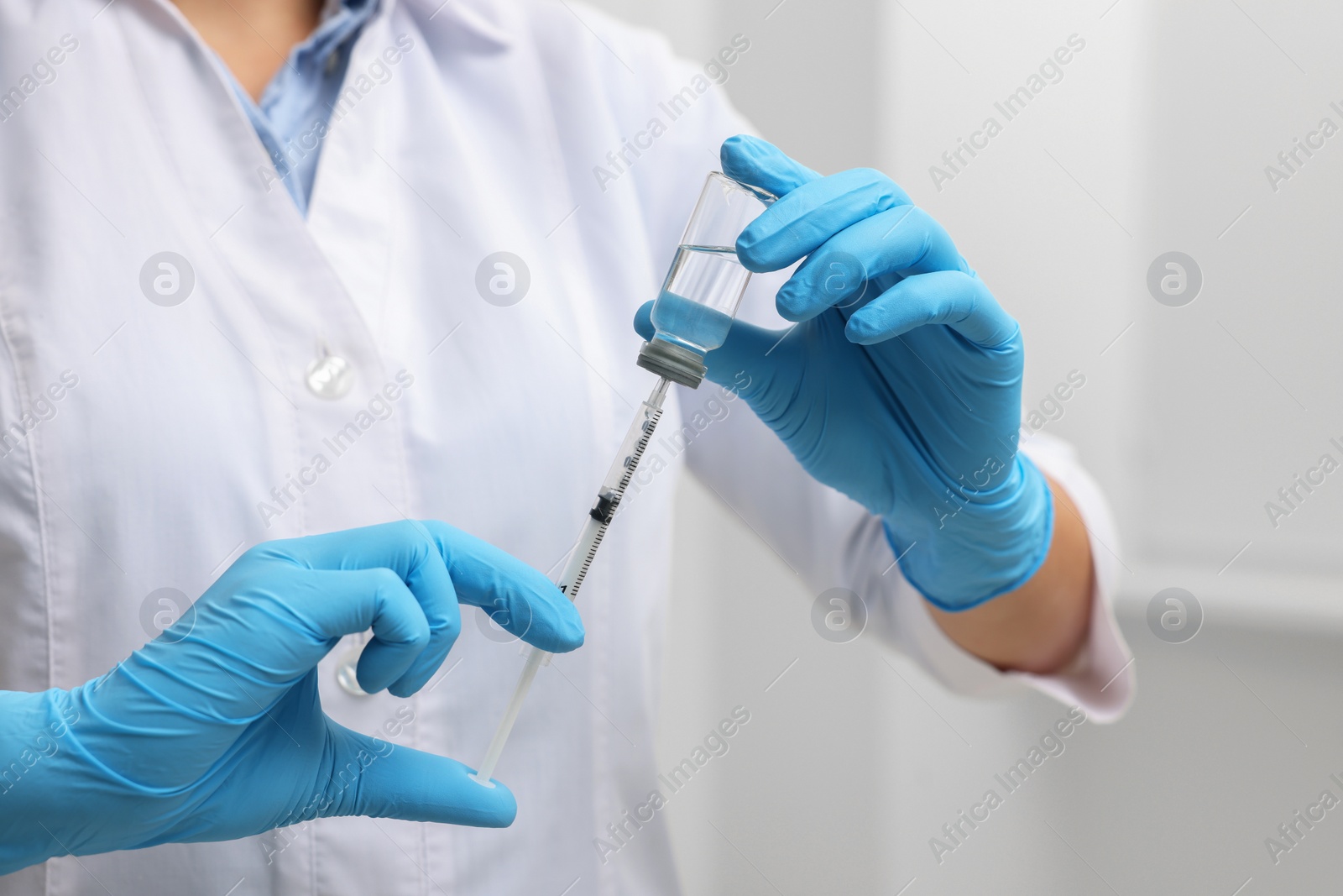 Photo of Doctor filling syringe with medication from glass vial indoors, closeup