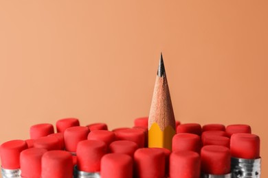 Sharp graphite pencil among others with erasers on brown background, closeup. Space for text