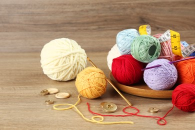 Photo of Clews of colorful knitting threads, crochet hooks, measuring tape and buttons on wooden table