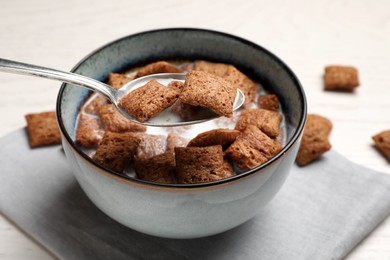 Photo of Spoon with tasty corn pads and milk over bowl at white table, closeup