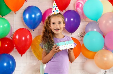 Photo of Happy girl with gift box at birthday party indoors