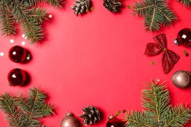 Photo of Frame of fir branches and Christmas decoration on red background, flat lay. Space for text