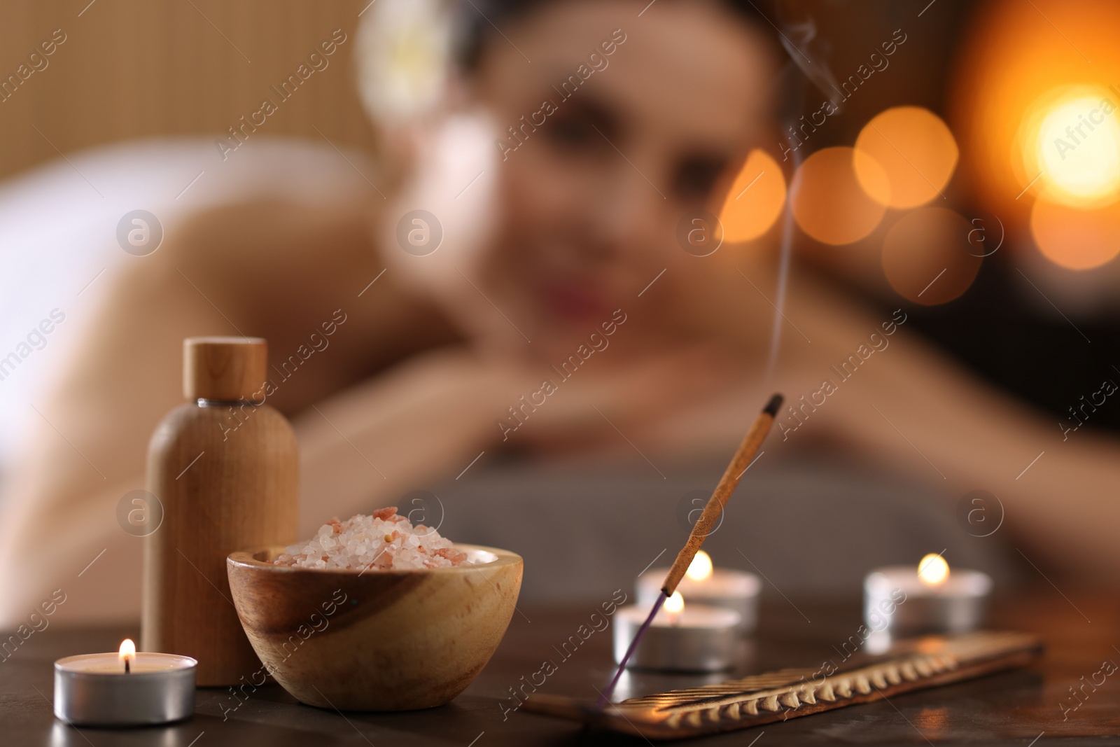 Photo of Spa therapy. Beautiful young woman lying on massage table in salon, focus on burning candles, salt and incense stick