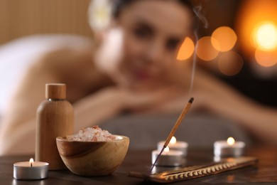 Spa therapy. Beautiful young woman lying on massage table in salon, focus on burning candles, salt and incense stick