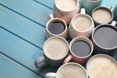 Many cups of different coffee drinks on light blue wooden table, above view