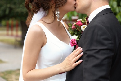 Young woman in wedding gown kissing her fiance outdoors