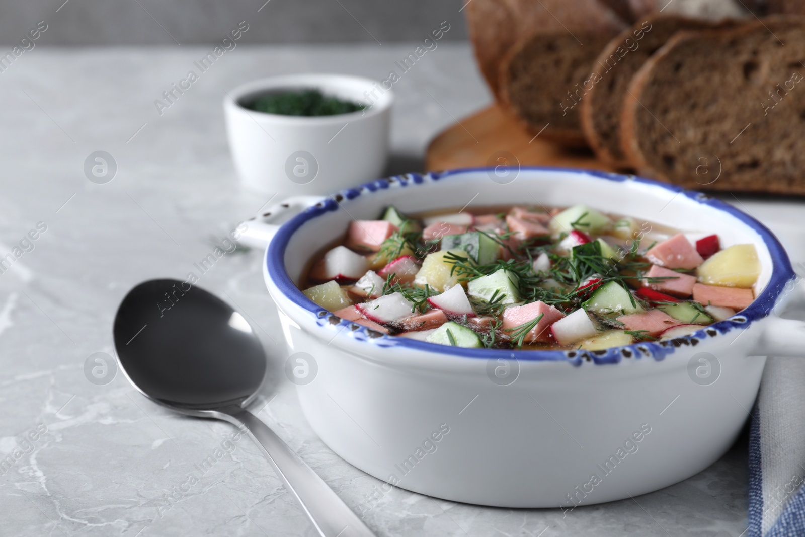 Photo of Delicious cold okroshka with kvass served on grey table, closeup. Traditional Russian summer soup