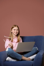 Photo of Cute teenage blogger with laptop sitting in armchair against color wall