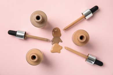 Photo of Bottles of liquid foundation and droppers on pink background, flat lay