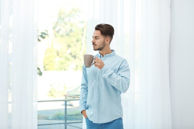 Young man standing near window with beautiful curtains at home