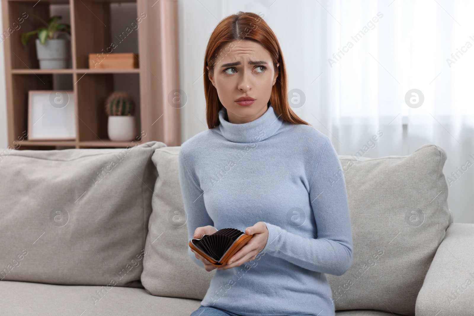 Photo of Upset woman with empty wallet on sofa indoors