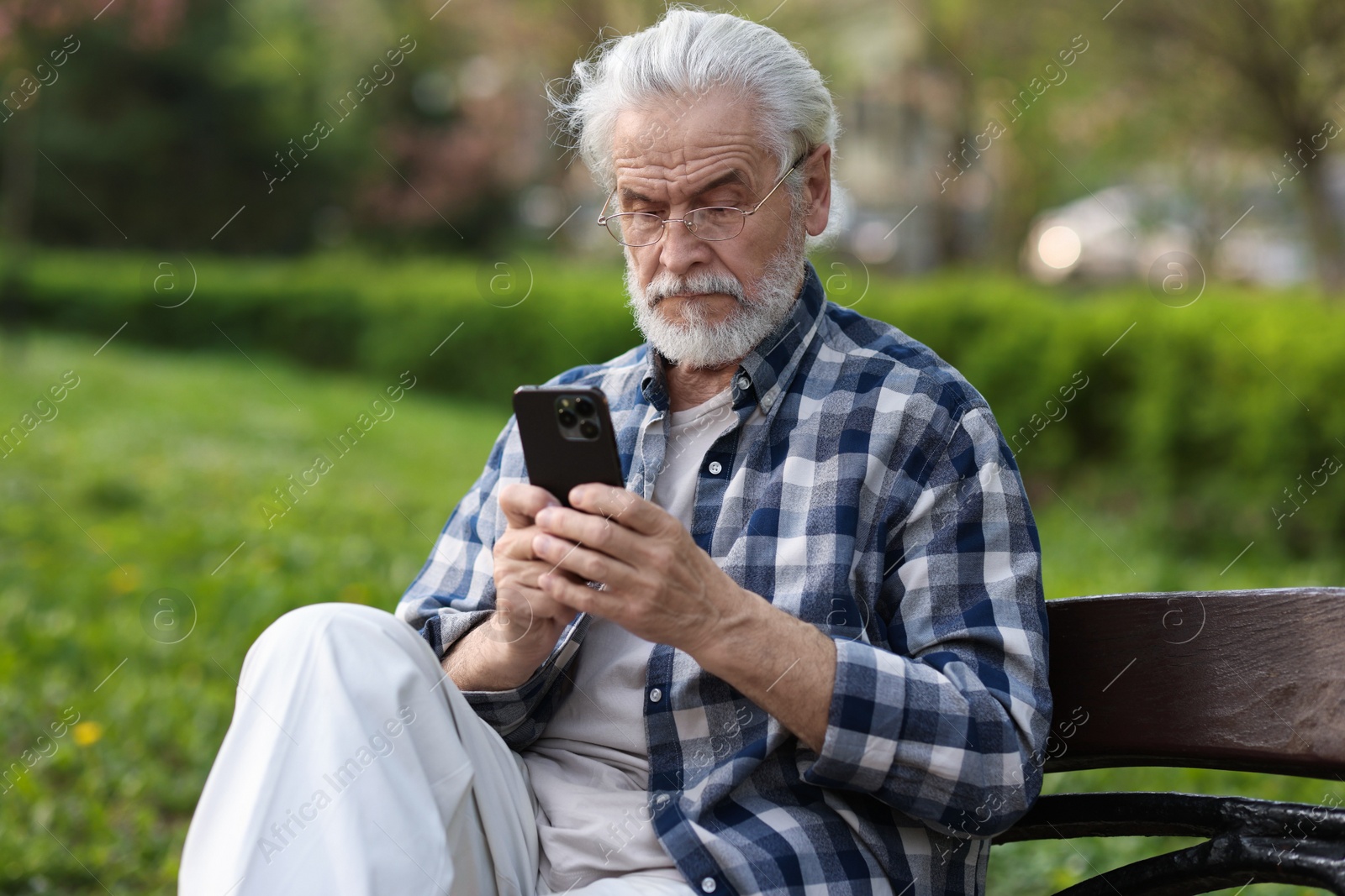 Photo of Portrait of happy grandpa with glasses using smartphone on bench in park