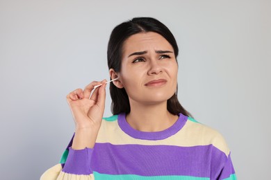 Photo of Young woman cleaning ear with cotton swab on light grey background
