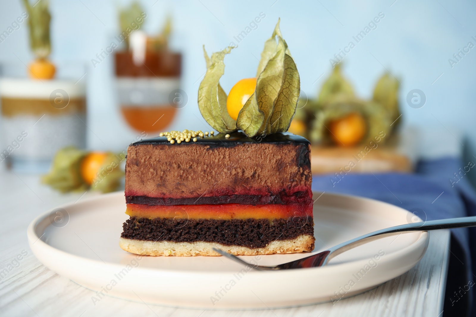 Photo of Piece of tasty cake decorated with physalis fruit on white wooden table