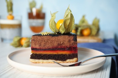 Piece of tasty cake decorated with physalis fruit on white wooden table