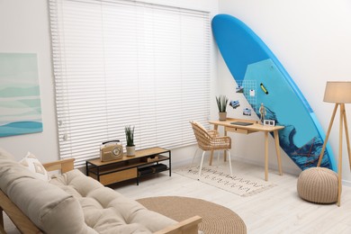 Photo of SUP board, workplace and sofa in room. Interior design