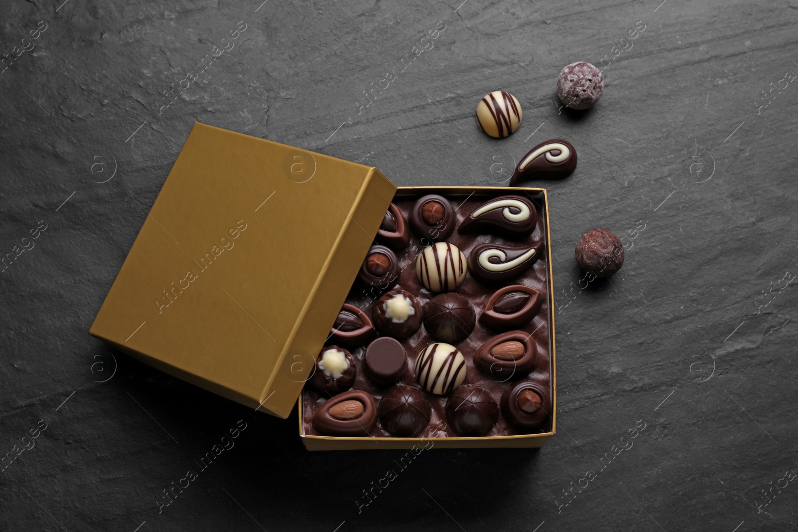 Photo of Open box of delicious chocolate candies on black table, flat lay