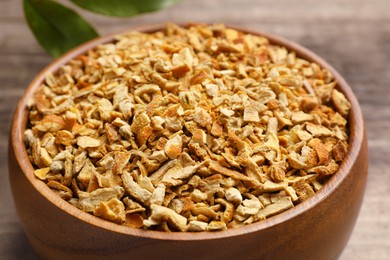 Photo of Bowl of dried orange zest seasoning and fresh leaves on wooden table, closeup