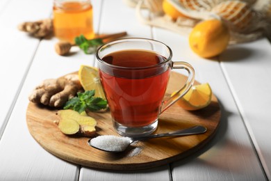 Cup of delicious ginger tea and ingredients on white wooden table, closeup