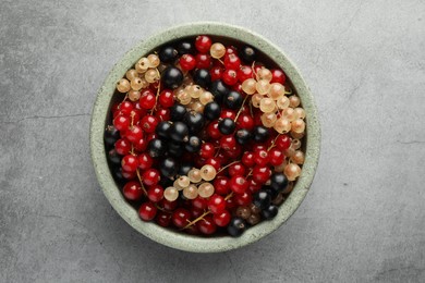 Photo of Different fresh ripe currants in bowl on light grey table, top view