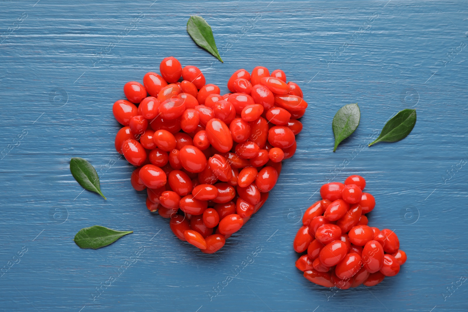 Photo of Heart shaped piles of fresh ripe goji berries on blue wooden table, flat lay