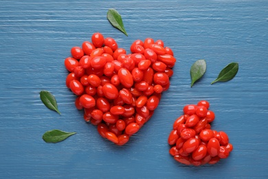 Heart shaped piles of fresh ripe goji berries on blue wooden table, flat lay