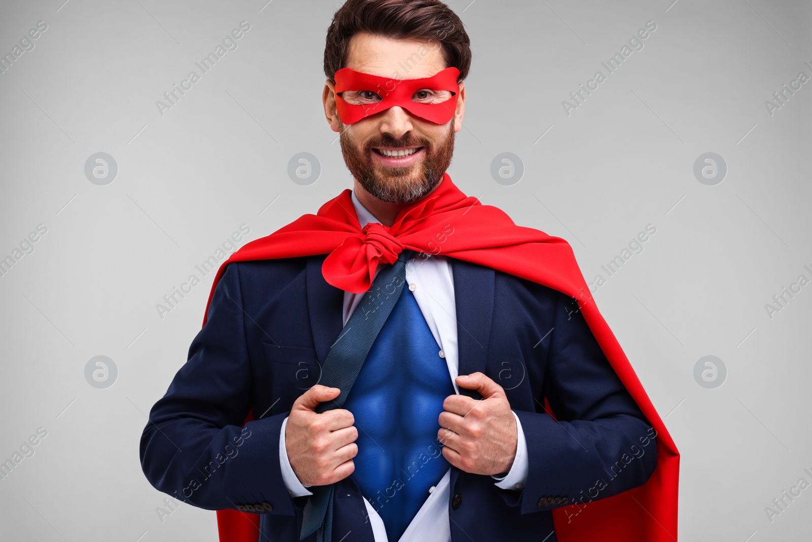 Image of Happy businessman wearing superhero costume under suit on light grey background