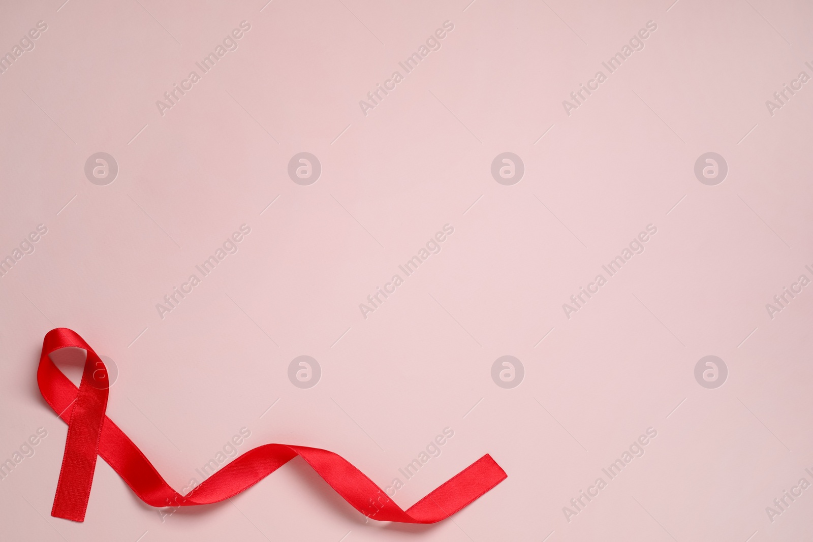 Photo of Top view of red ribbon on pink background, space for text. AIDS disease awareness