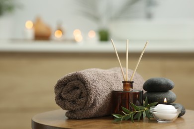 Photo of Spa composition. Rolled towel, aroma diffuser, massage stones and burning candle on wooden table indoors. Space for text