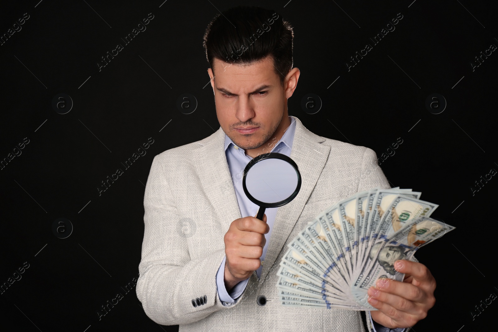 Photo of Expert authenticating 100 dollar banknotes with magnifying glass against black background. Fake money concept