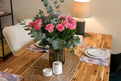 Beautiful table setting with bouquet and candles indoors. Roses and eucalyptus branches in vase