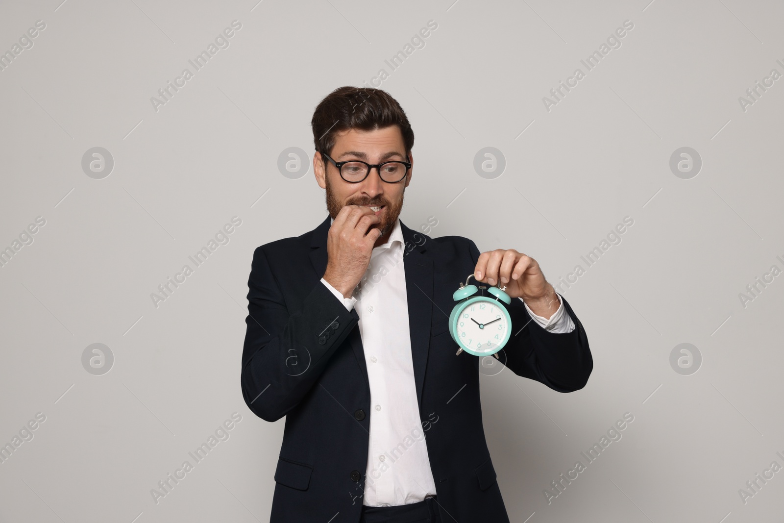 Photo of Emotional bearded man with alarm clock on light grey background. Being late concept