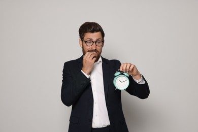 Emotional bearded man with alarm clock on light grey background. Being late concept