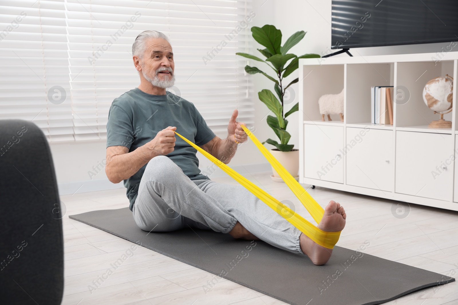 Photo of Senior man doing exercise with fitness elastic band on mat at home