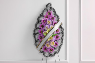 Funeral wreath of plastic flowers with ribbon near white wall