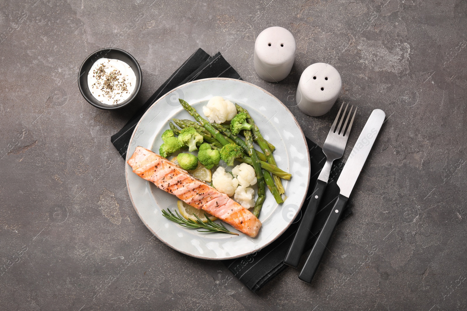 Photo of Healthy meal. Piece of grilled salmon, vegetables, asparagus and rosemary served with sauce on grey textured table, flat lay