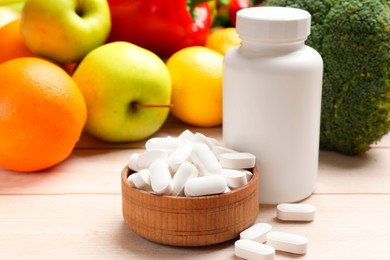 Photo of Dietary supplements. Bottle and bowl with pills near food products on light wooden table, closeup