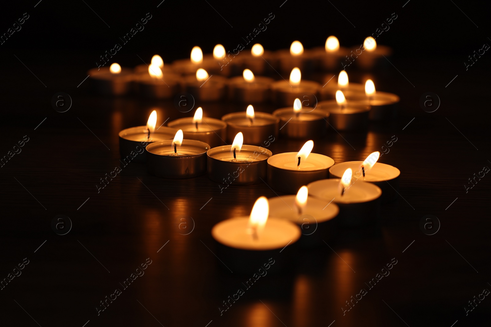 Photo of Burning candles on surface in darkness, closeup