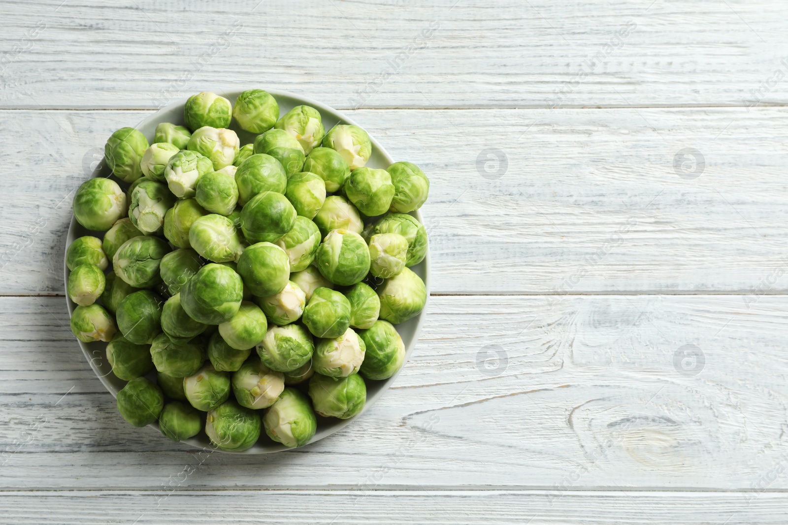 Photo of Plate with fresh Brussels sprouts on wooden background, top view. Space for text