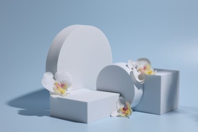 Photo of Scene for product presentation. Podiums of different geometric shapes and orchid flowers on light blue background