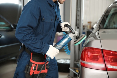 Photo of Technician polishing car body with tool at automobile repair shop, closeup