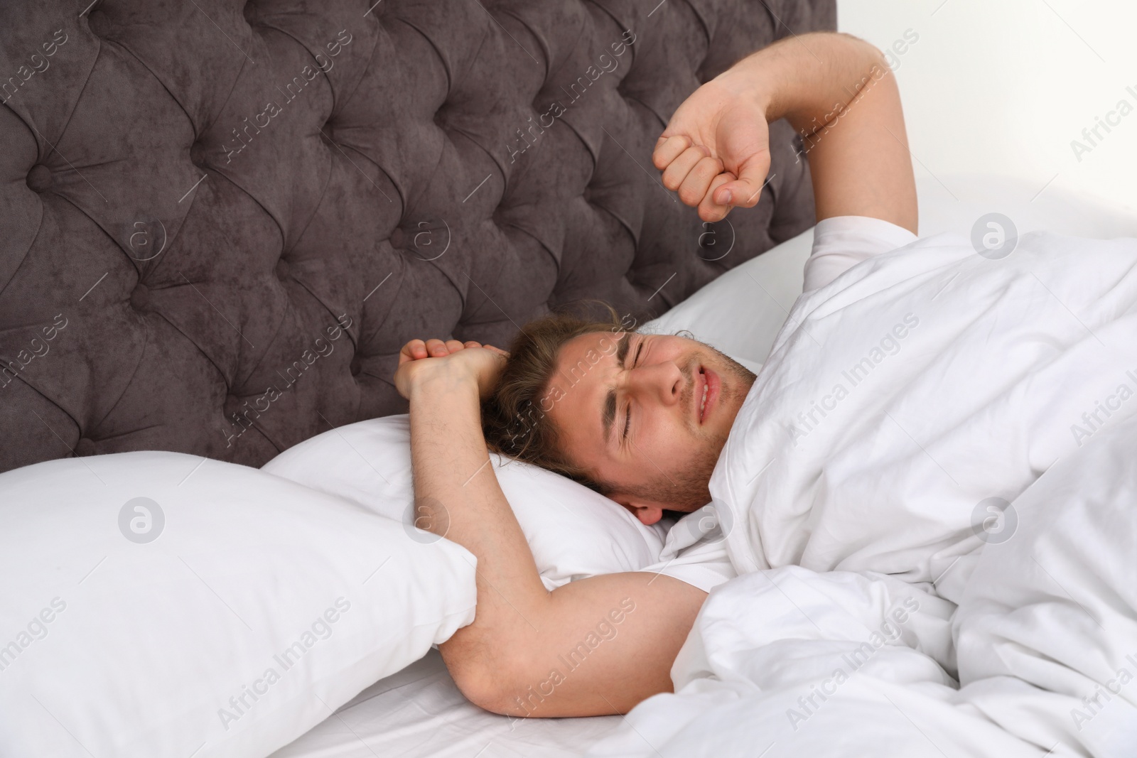 Photo of Handsome young man stretching while lying under blanket at home. Bedtime