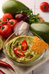 Photo of Bowl of delicious guacamole, nachos chip and ingredients on table