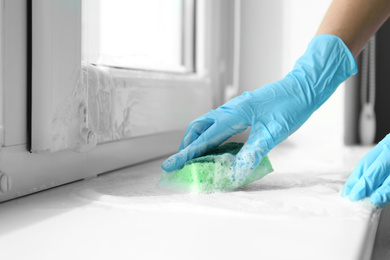 Photo of Woman cleaning window sill with sponge, closeup