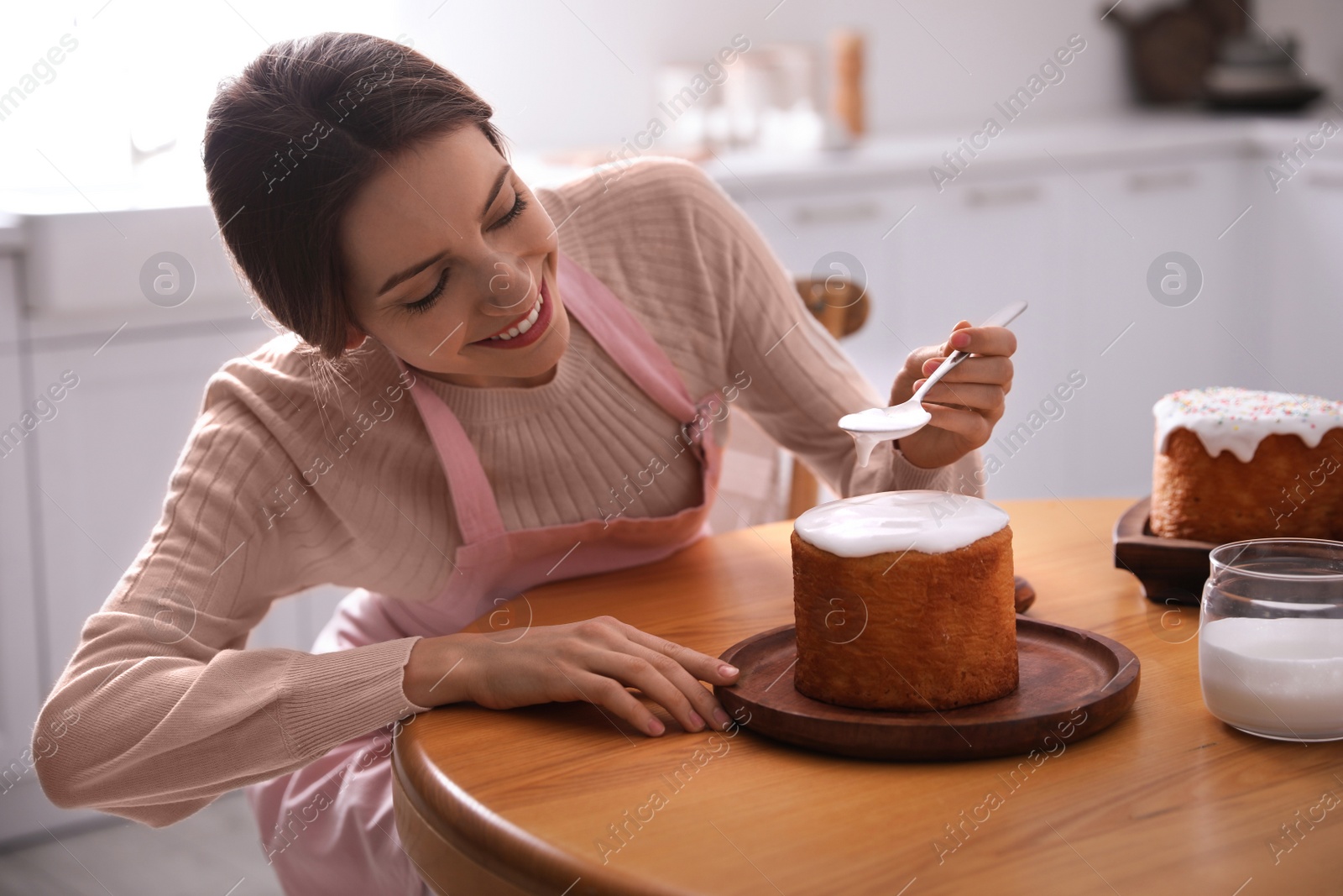 Photo of Young woman decorating traditional Easter cake with glaze in kitchen