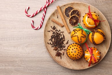 Photo of Pomander balls made of tangerines with cloves and candy canes on wooden table, flat lay. Space for text