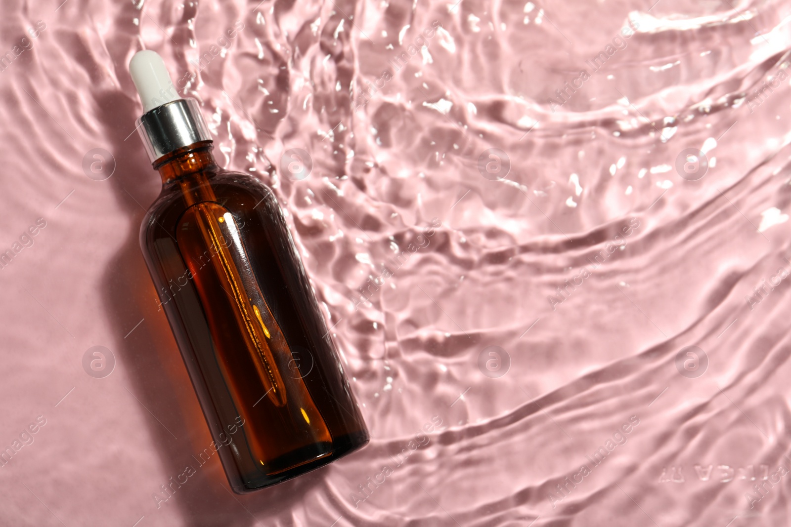 Photo of Bottle of hydrophilic oil in water on pink background, top view. Space for text