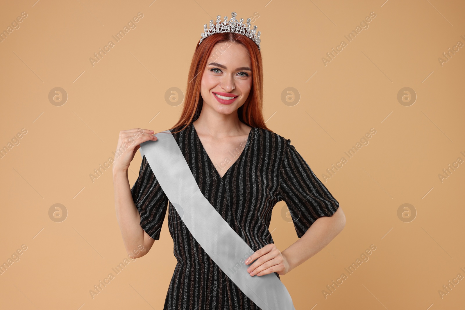 Photo of Beautiful young woman with tiara and ribbon in dress on beige background. Beauty contest