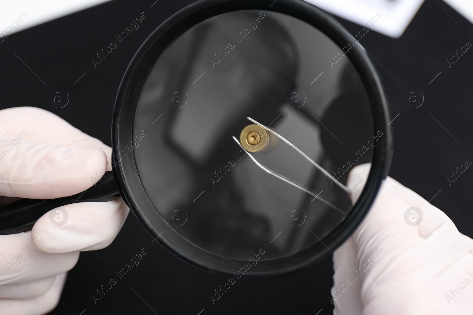 Photo of Detective exploring bullet shell with magnifying glass on black background, closeup