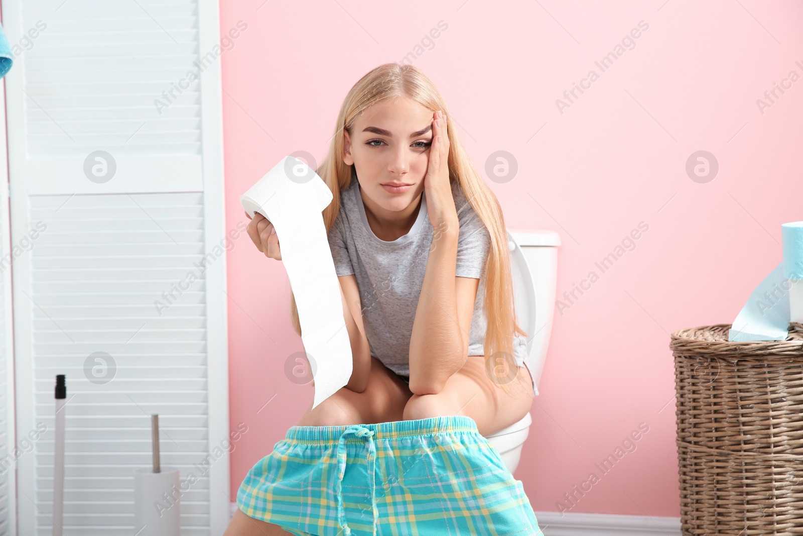 Photo of Woman with paper roll sitting on toilet bowl in bathroom